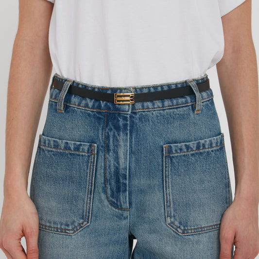 Close-up of a person wearing blue denim jeans with a Victoria Beckham Exclusive Micro Frame Belt in black leather, focusing on the back pockets and belt area.