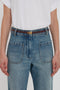 Person wearing a white t-shirt tucked into high-waisted blue jeans with large front pockets, complemented by a luxurious Victoria Beckham Exclusive Micro Frame Belt In Burgundy Leather.