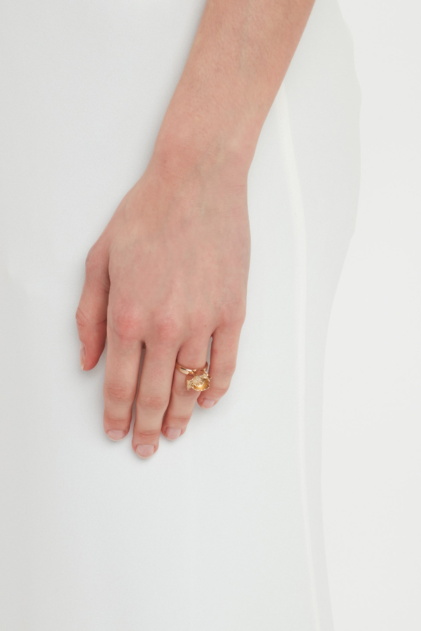 Close-up of a hand wearing a Victoria Beckham Exclusive Camellia Flower Ring In Gold, resting on white fabric, beautifully handcrafted in Italy.