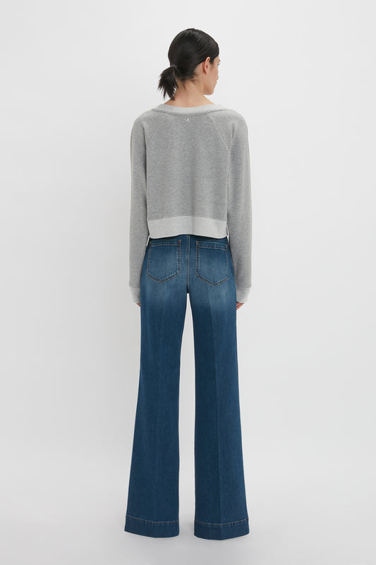 Sentence with product replaced:
Rear view of a woman wearing a Victoria Beckham Cropped Sweatshirt in Grey Marl and blue flared jeans standing against a white background.