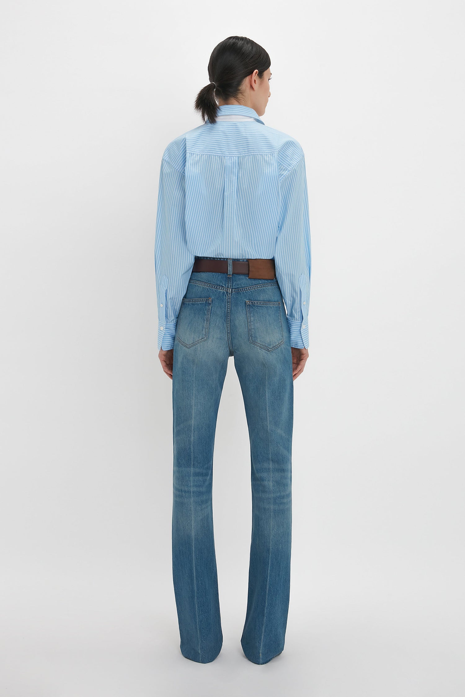 Person wearing a Cropped Long Sleeve Shirt In Marina-White by Victoria Beckham and blue jeans, viewed from the back, standing against a plain white background.