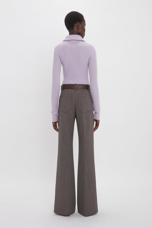 A person stands with their back facing the camera, wearing a Victoria Beckham Double Collared Jumper In Petunia and high-waisted brown wide-legged pants.