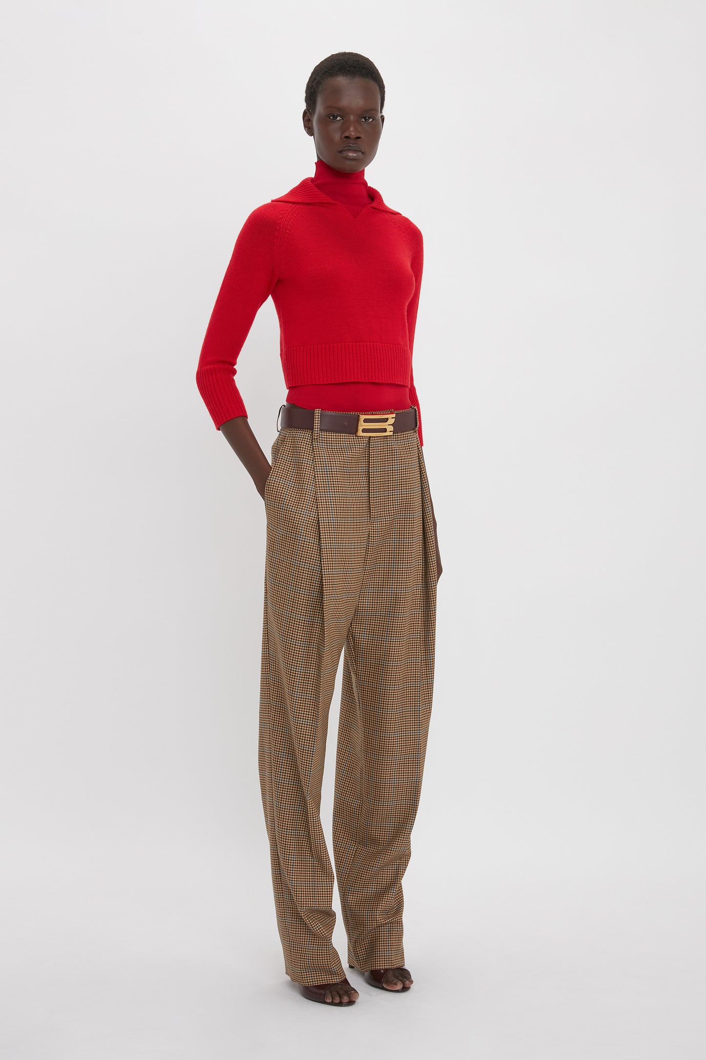 Person wearing a Victoria Beckham Double Layer Top In Deep Red and brown plaid wide-leg trousers with a brown belt, standing against a white background.