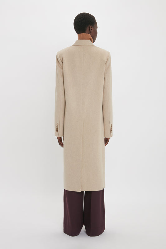 A person seen from the back, wearing a Victoria Beckham tailored slim coat in bone and dark burgundy trousers, standing against a white background.