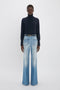 Person wearing a dark turtleneck and Alina High Waisted Jean In Light Summer Wash by Victoria Beckham stands against a plain white background.