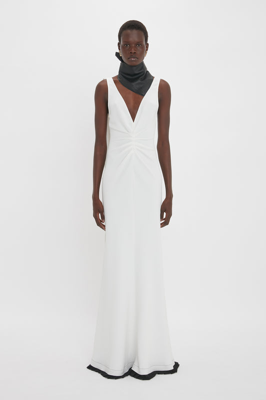 A person stands facing forward, wearing an elegant Exclusive V-Neck Gathered Waist Floor-Length Gown In Ivory by Victoria Beckham with a deep V-neck and a black neckpiece, accentuating the hourglass silhouette.