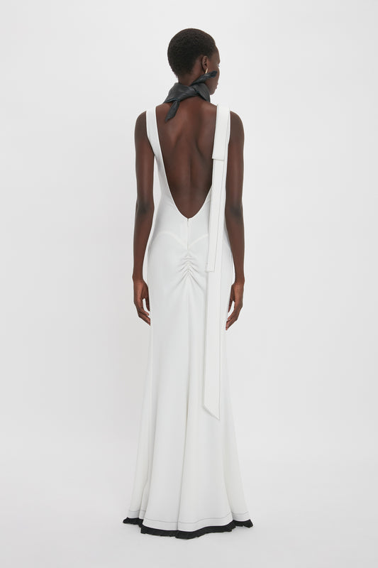 A person wearing the Victoria Beckham Exclusive V-Neck Gathered Waist Floor-Length Gown In Ivory, with a low back and black neck tie, showcasing an hourglass silhouette, photographed from behind against a plain white background.