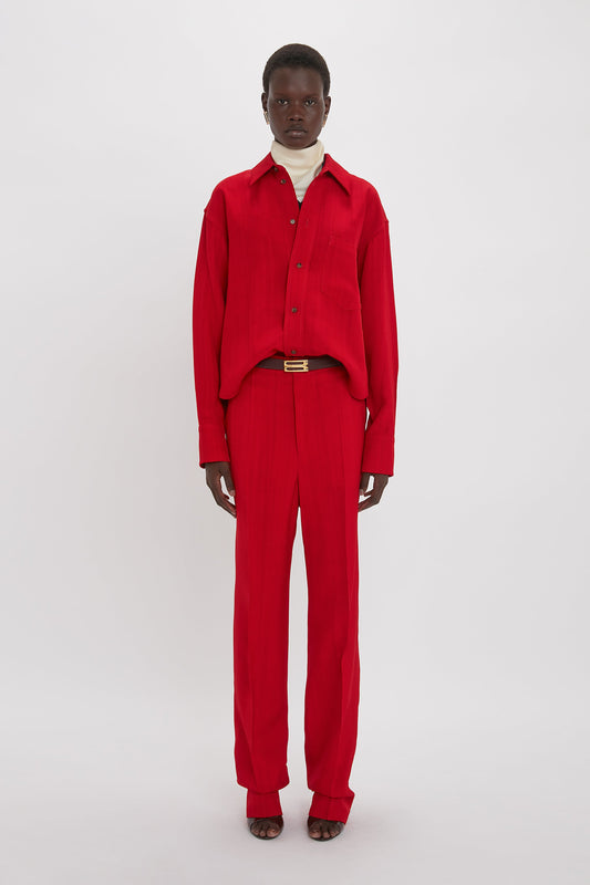 The individual sports a Victoria Beckham Cropped Long Sleeve Shirt In Carmine paired with matching red trousers, standing against a plain white background.