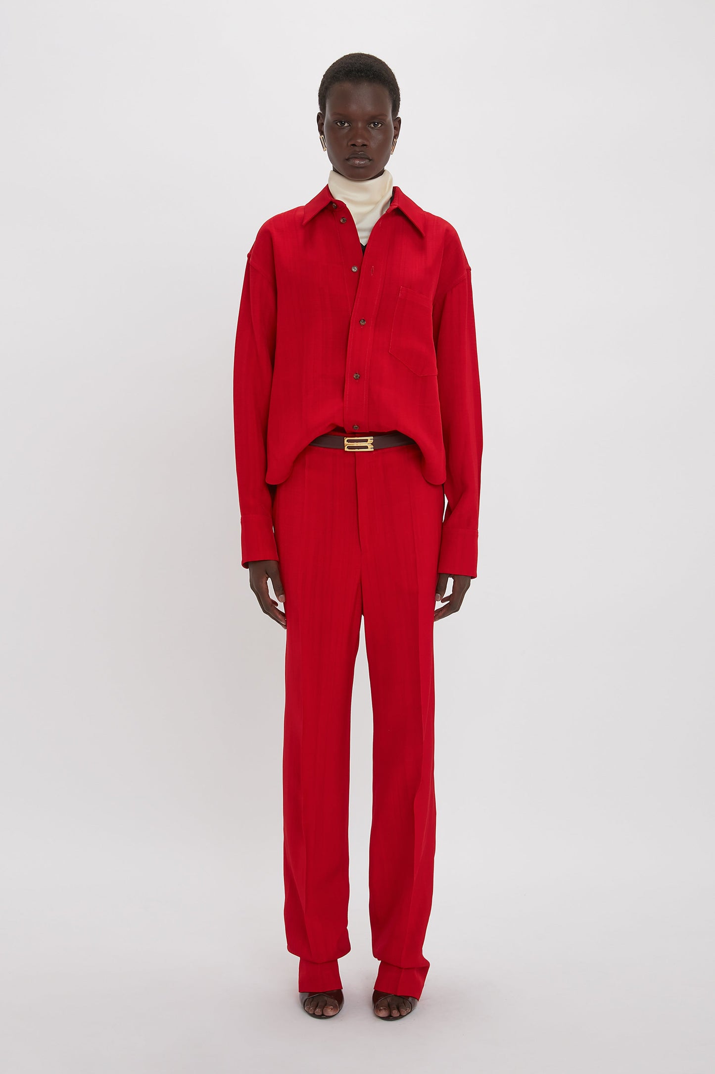 Person wearing a red button-up shirt and Victoria Beckham's Tapered Leg Trouser In Carmine, standing against a plain white background, showcasing a lean silhouette and refined traditional tailoring.