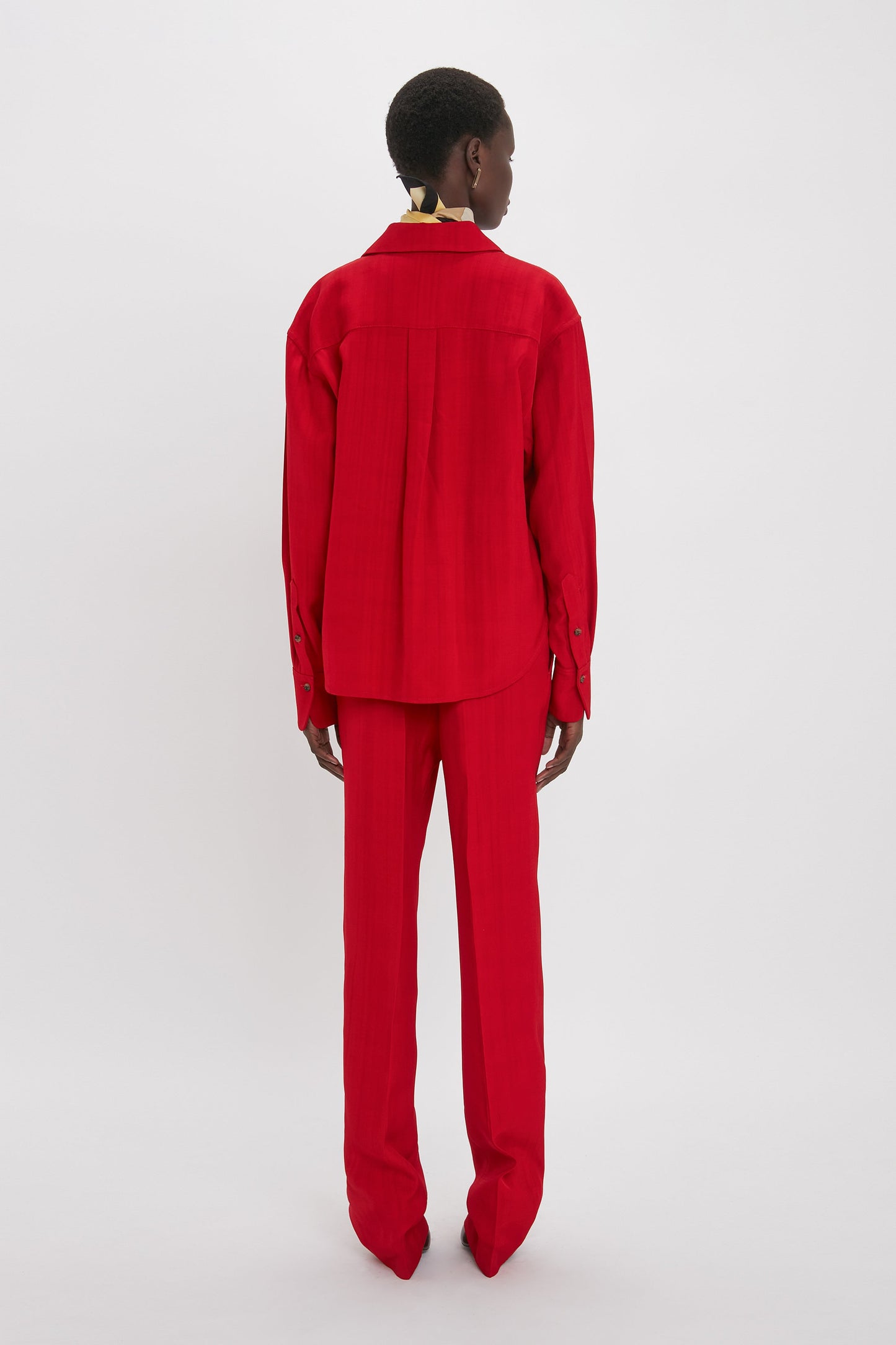 Person is standing facing away, wearing a bright red Victoria Beckham Cropped Long Sleeve Shirt In Carmine and matching red pants against a plain white background.