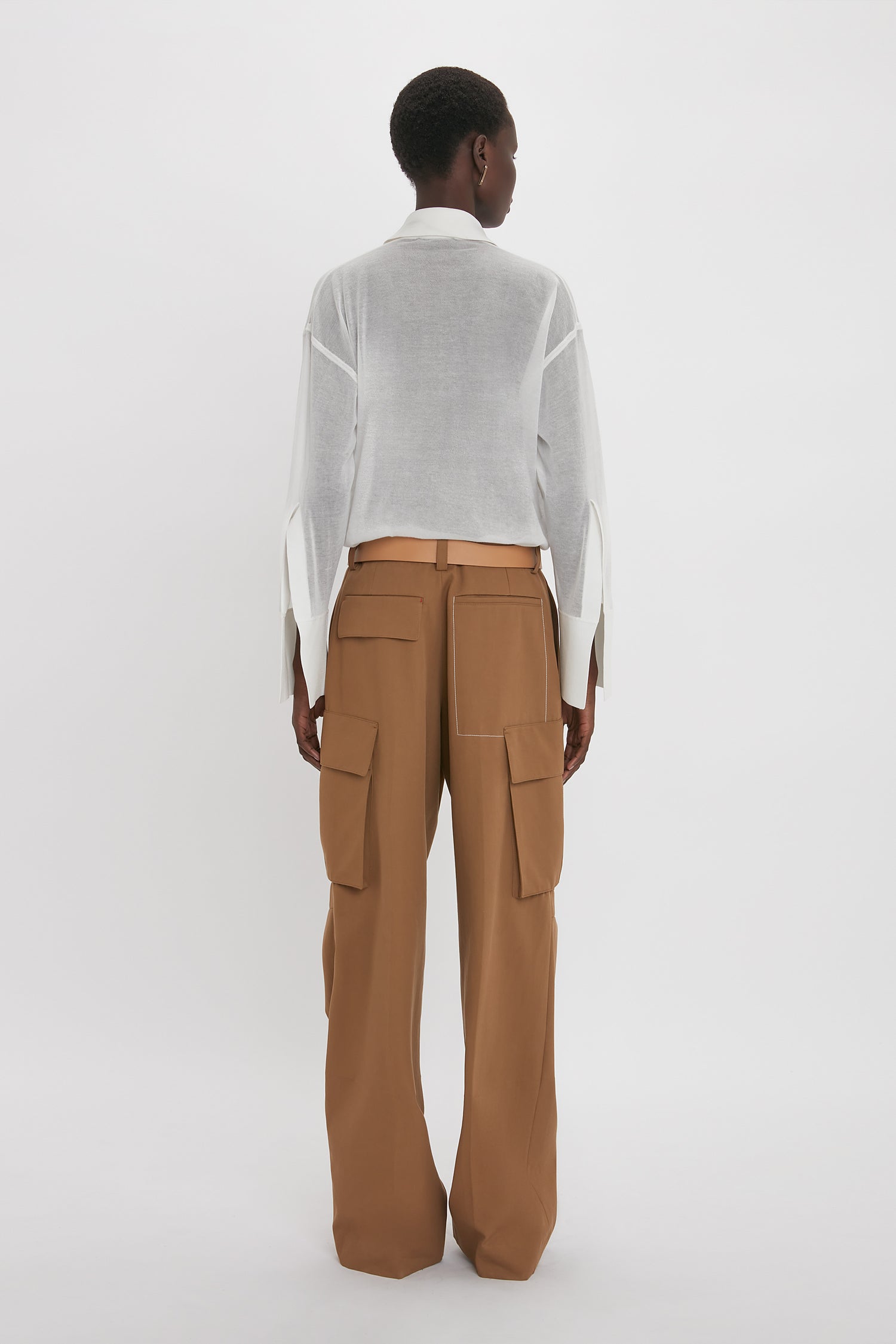 Person facing away, wearing a relaxed fit Pocket Detail Shirt In White by Victoria Beckham with tan cargo pants with large pockets, standing against a plain white background. The casual sophistication of the ensemble is evident in the understated yet stylish choices.