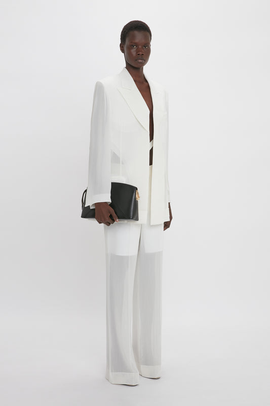 Person standing against a plain white background, wearing the **Fold Detail Tailored Jacket In White** from **Victoria Beckham**, with featherweight wool pantsuit and double-breasted cut, holding a black clutch bag.