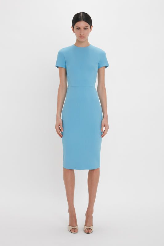 A woman in a Victoria Beckham Exclusive Fitted T-Shirt Dress In Periwinkle Blue with short sleeves and heeled sandals stands against a plain white background.