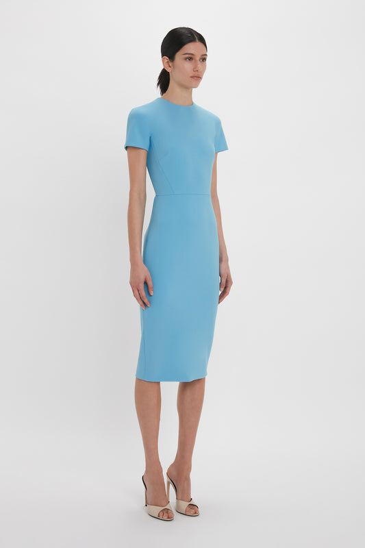 A woman in an Exclusive Fitted T-Shirt Dress In Periwinkle Blue by Victoria Beckham, paired with silver heels, standing against a white background.