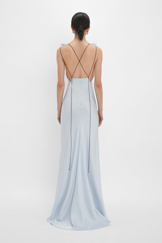 A person in an elegant, ice blue Exclusive Gathered Shoulder Cami Floor-Length Gown In Ice Blue by Victoria Beckham with an open back and crisscrossed thin black straps stands facing away against a plain white background. The stunning crepe back satin fabric gracefully accentuates the figure.