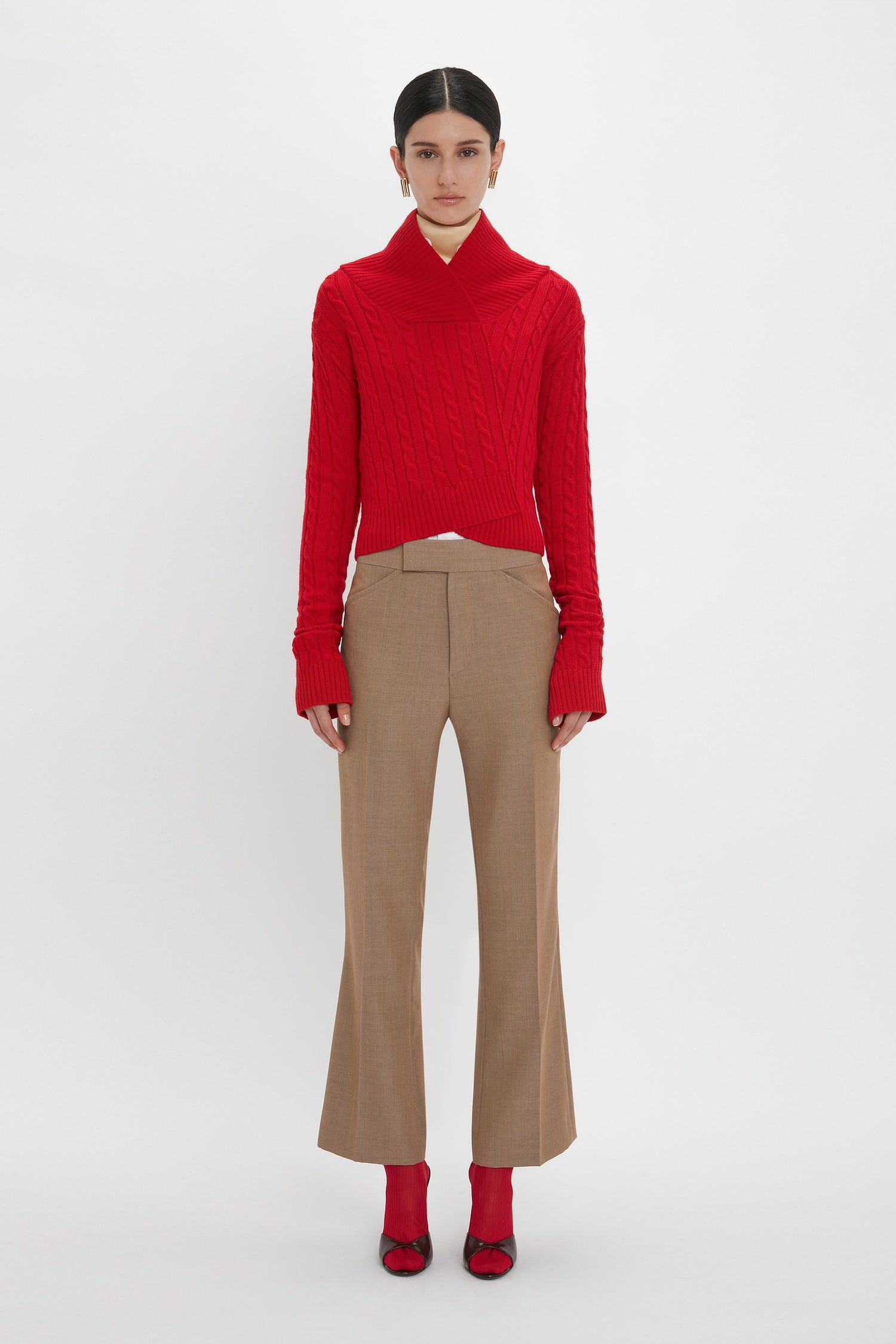 A person is standing against a plain background wearing a red sweater, Victoria Beckham Wide Cropped Flare Trouser In Tobacco that offer a flattering hint of ankle, and matching red shoes.