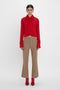 Person wearing a Wrap Detail Jumper In Red from the Victoria Beckham brand, tan pants, and red shoes stands against a plain white background.