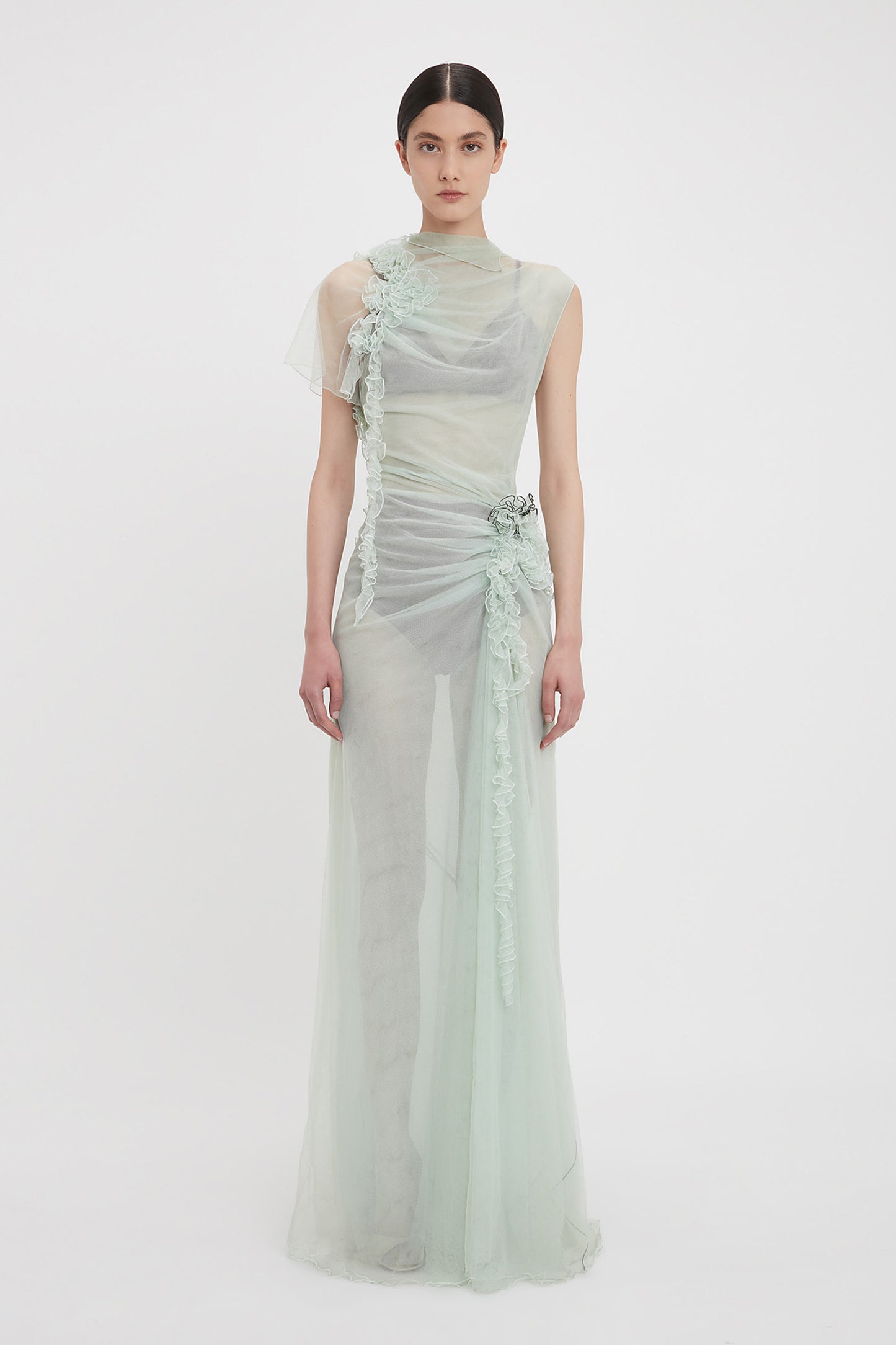A person stands wearing the Victoria Beckham Gathered Tulle Detail Floor-Length Dress In Jade, set against a plain white background.