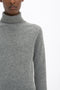 Person wearing a Polo Neck Jumper In Grey Melange by Victoria Beckham against a white background. Only the upper body and part of the face are visible. The versatile styling evokes a timeless elegance reminiscent of Victoria Beckham's monogram designs.