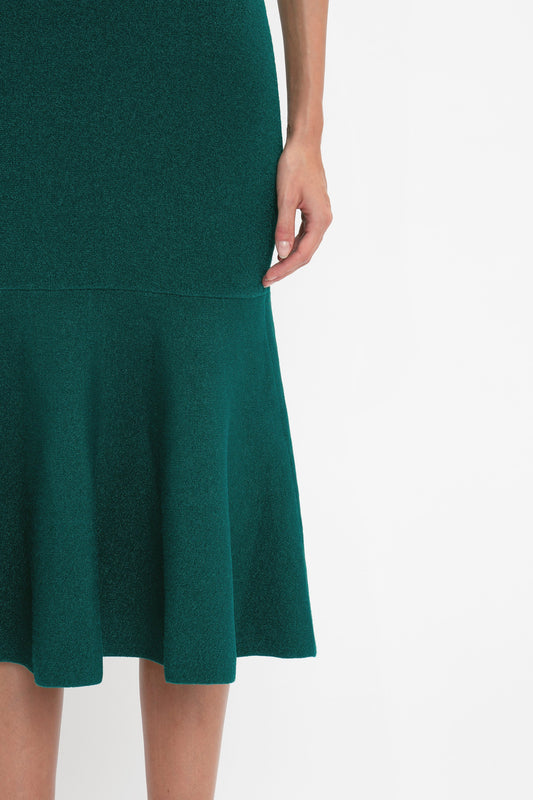 A close-up of a person wearing a fitted Victoria Beckham VB Body Sleeveless Dress In Lurex Green with a flared silhouette. Only the lower torso and one arm are visible against a plain white background, making it perfect for your new-season wardrobe.
