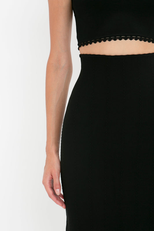 A person wearing a black top and Victoria Beckham VB Body Scallop Trim Flared Skirt In Black; the image shows the person's upper left arm and torso.