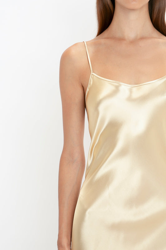 Close-up of a person wearing the Victoria Beckham Exclusive Floor-Length Cami Dress In Gold with thin straps and 1990s-inspired charm against a white background.
