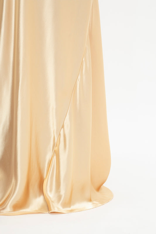 Close-up view of the lower part of a flowing, satin-like, Exclusive Floor-Length Cami Dress In Gold by Victoria Beckham against a plain white background.