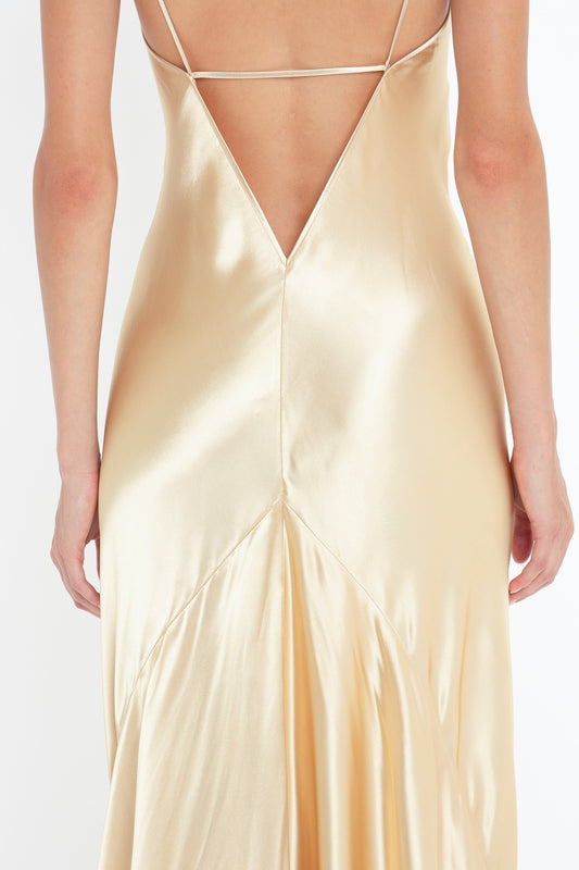 Back view of a person wearing a 1990s-inspired gold, satin Exclusive Floor-Length Cami Dress In Gold by Victoria Beckham with thin straps and a low V-cut back.