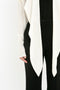 Close-up of a person wearing an Oversized Bow Detail Blouse In Vanilla by Victoria Beckham paired with high-waisted black pants against a plain background. Only the torso and upper legs are visible, adding a dramatic finishing touch to the ensemble.