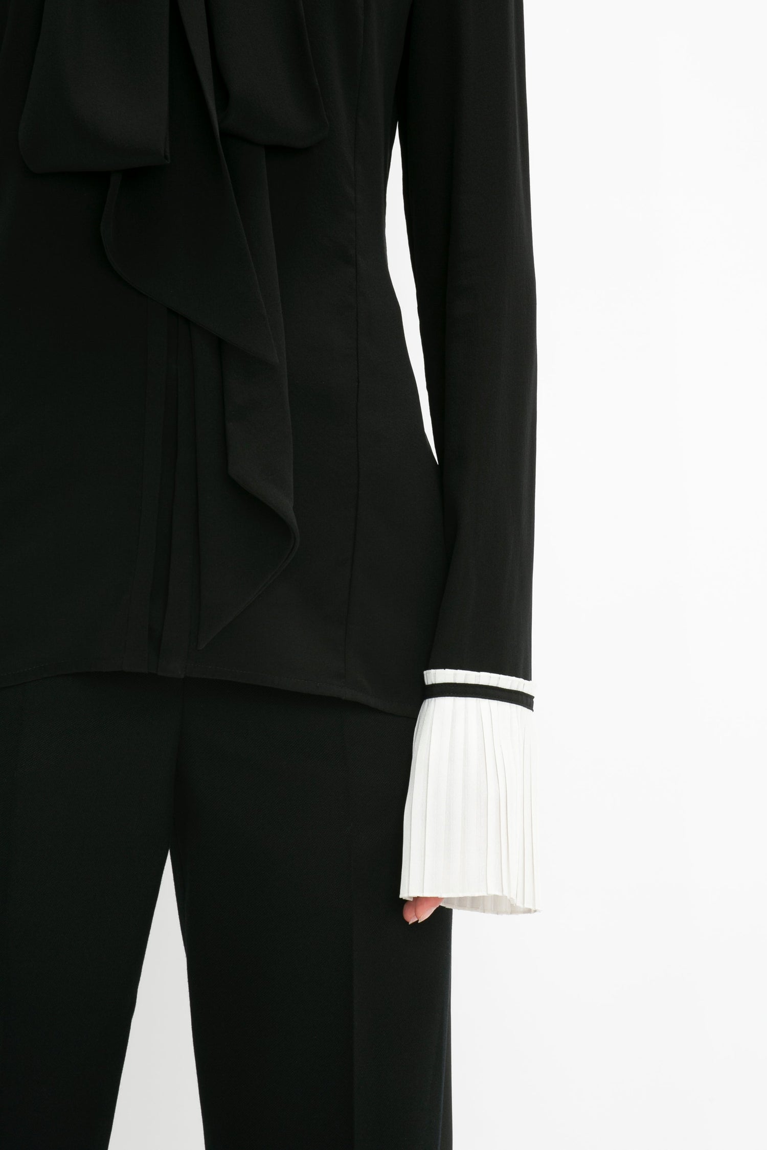 A person wearing the Pleat Cuff Blouse In Black by Victoria Beckham with knife pleat cuffs and a white pleated cuff detail on the sleeve.