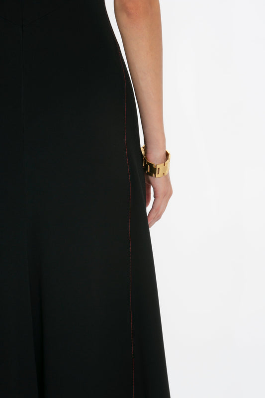 Side view close-up of a woman wearing a Victoria Beckham short sleeve tie detail dress in black with red seam detail, and a gold bracelet, against a white background.