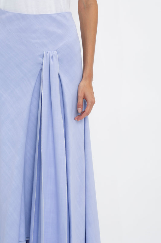 A person wearing a white top and a light blue Asymmetric Tie Detail Skirt In Frost by Victoria Beckham in viscose crepe fabric, showcasing modern femininity with pleated detail, showing their arm and part of their hand.