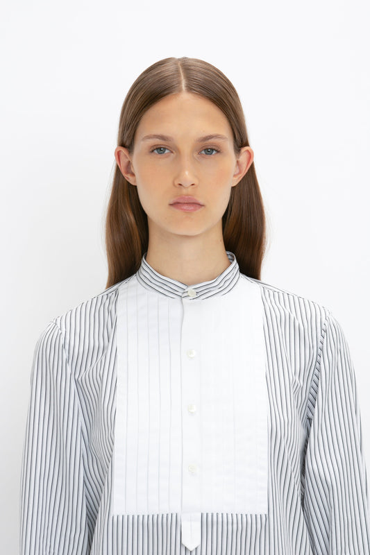 A person with long brown hair and a neutral expression wears the Tuxedo Bib Shirt in Black and Off-White by Victoria Beckham, showcasing a relaxed look. The outfit, inspired by classic menswear silhouettes, stands out against the plain white background.