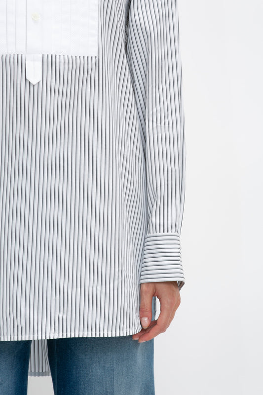 Close-up of a person wearing a Victoria Beckham Tuxedo Bib Shirt in Black and Off-White with white collar and cuffs. The hand is visible, resting casually by their side. Made from organic cotton, this piece pairs effortlessly with blue jeans for a relaxed look.