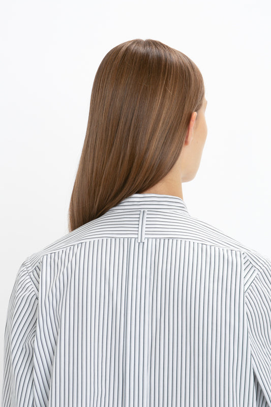 A person with straight, shoulder-length brown hair is shown from the back, wearing a Victoria Beckham Tuxedo Bib Shirt in Black and Off-White. The relaxed look of the organic cotton fabric adds a touch of effortless style.
