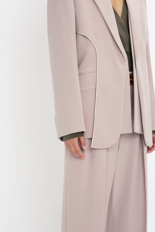 Person in a beige suit with white piping detail, wearing an olive green shirt underneath, adorned with the timeless elegance of the Double Panel Front Jacket In Rose Quartz by Victoria Beckham.