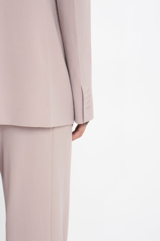 Close-up of a person wearing a Double Panel Front Jacket In Rose Quartz from the back. The image highlights the classic tailored jacket with its clean lines and subtle fabric texture, showcasing the lower part of the blazer and the upper part of the trousers. The ensemble is by Victoria Beckham.