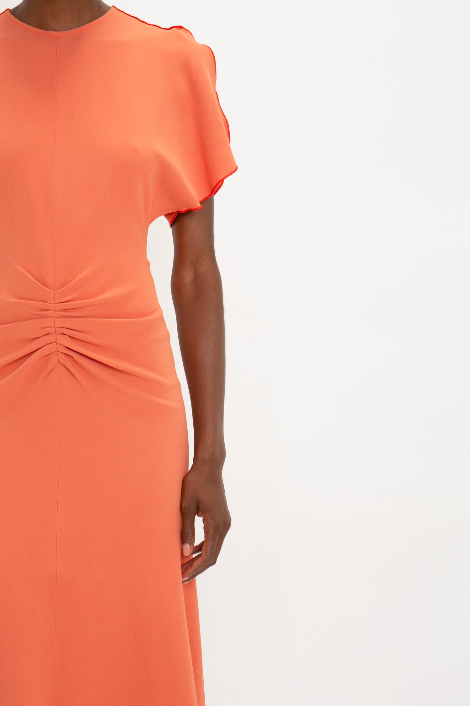 Woman wearing a bright Victoria Beckham papaya Gathered Waist Midi Dress with ruffled sleeves and a cinched waist detail, cropped to show from shoulders to mid-thigh.