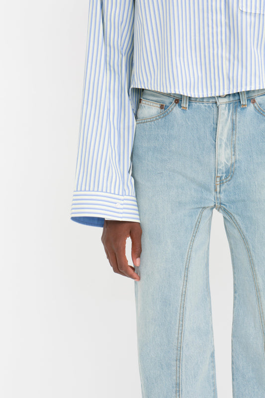 A person wearing a Victoria Beckham Button Detail Cropped Shirt In Chamomile Blue Stripe and light blue jeans demonstrates versatile styling.