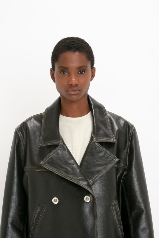 Person with short hair wearing a distressed finish Victoria Beckham Oversized Leather Jacket In Black over a light-colored top, standing against a plain white background.