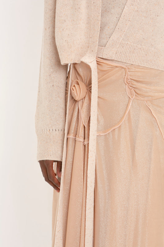 Close-up of a person wearing a light beige long-sleeve sweater with a button detail and a matching flowing Flower Detail Cami Skirt In Rosewater by Victoria Beckham featuring a delicate flower embellishment.