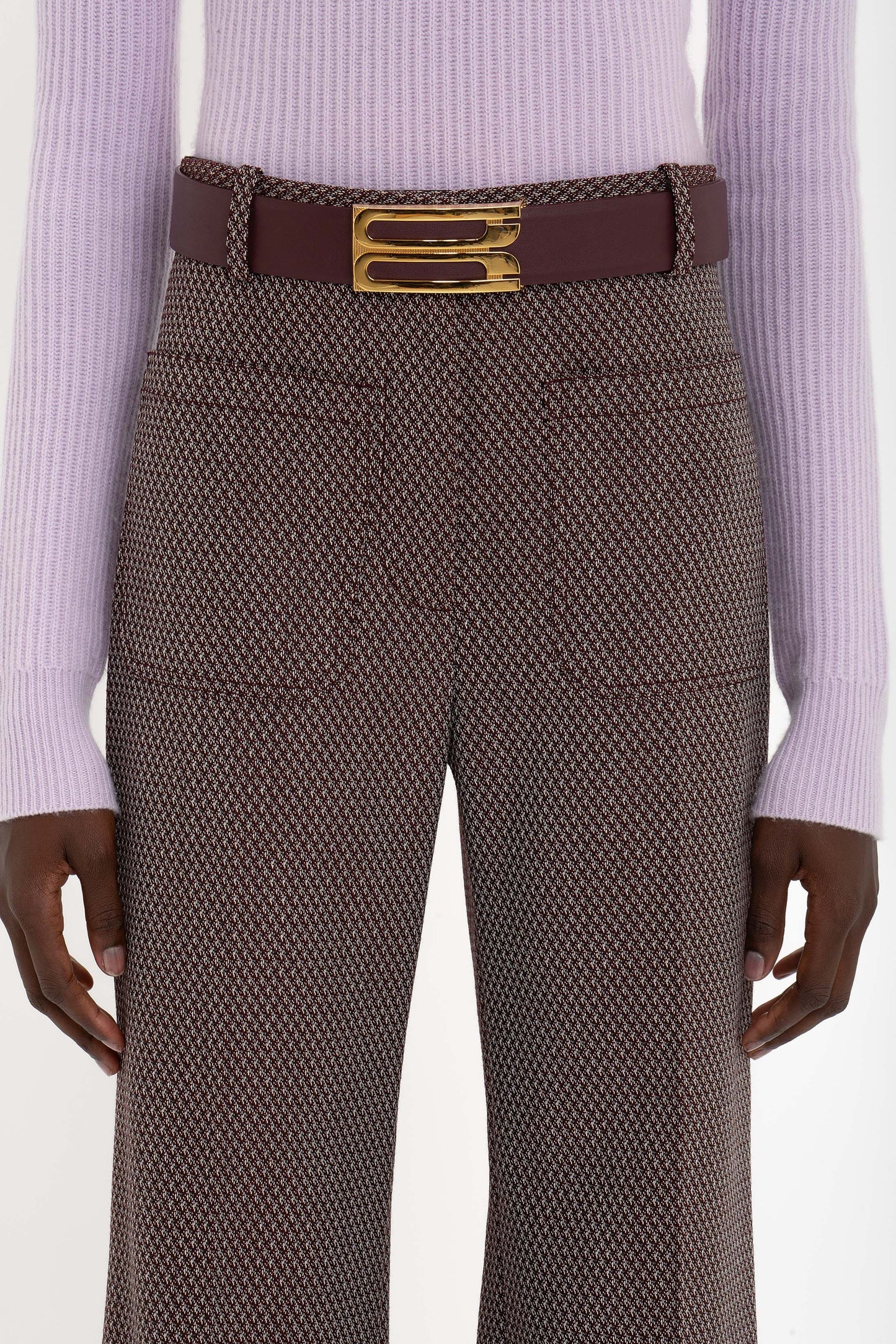 A person wearing a light purple long-sleeve top, high-waisted Alina Trouser In Tobacco by Victoria Beckham, and a burgundy belt with a gold buckle.