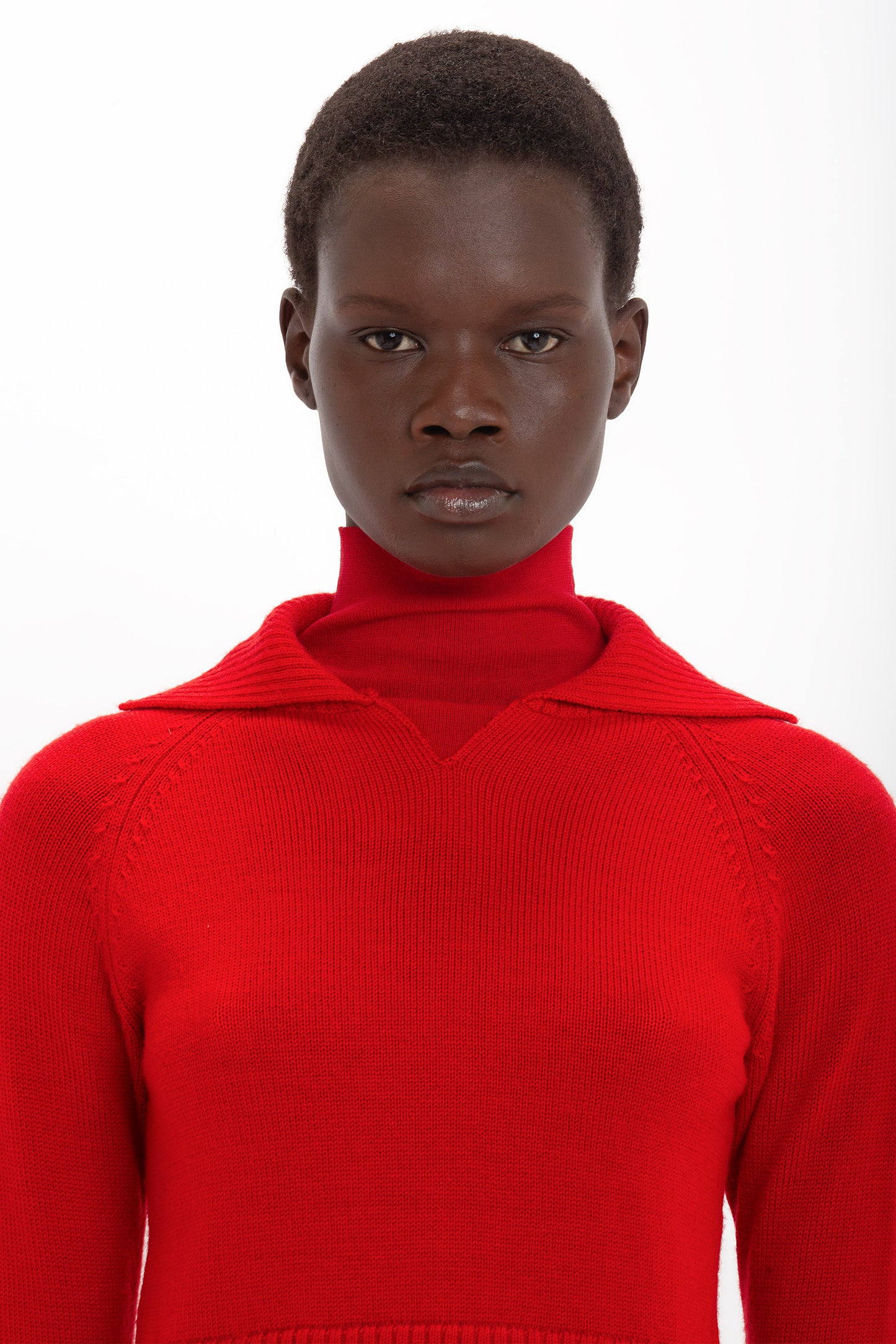 A person is wearing a vibrant red Double Layer Top In Deep Red crafted from soft merino wool, channeling a Victoria Beckham vibe. They have short hair and are looking directly at the camera against a plain white background.