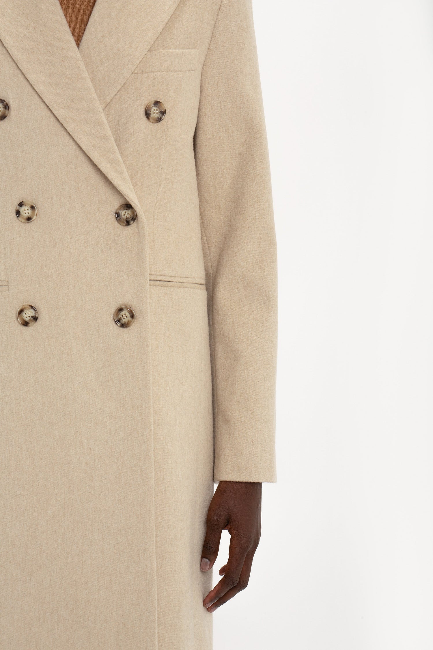 Close-up of a person wearing a Victoria Beckham Tailored Slim Coat In Bone, focusing on the coat's texture and buttons with a visible hand detail.