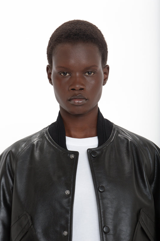 Person with short hair wearing a Victoria Beckham Leather Varsity Jacket In Black over a white shirt, standing against a plain white background.