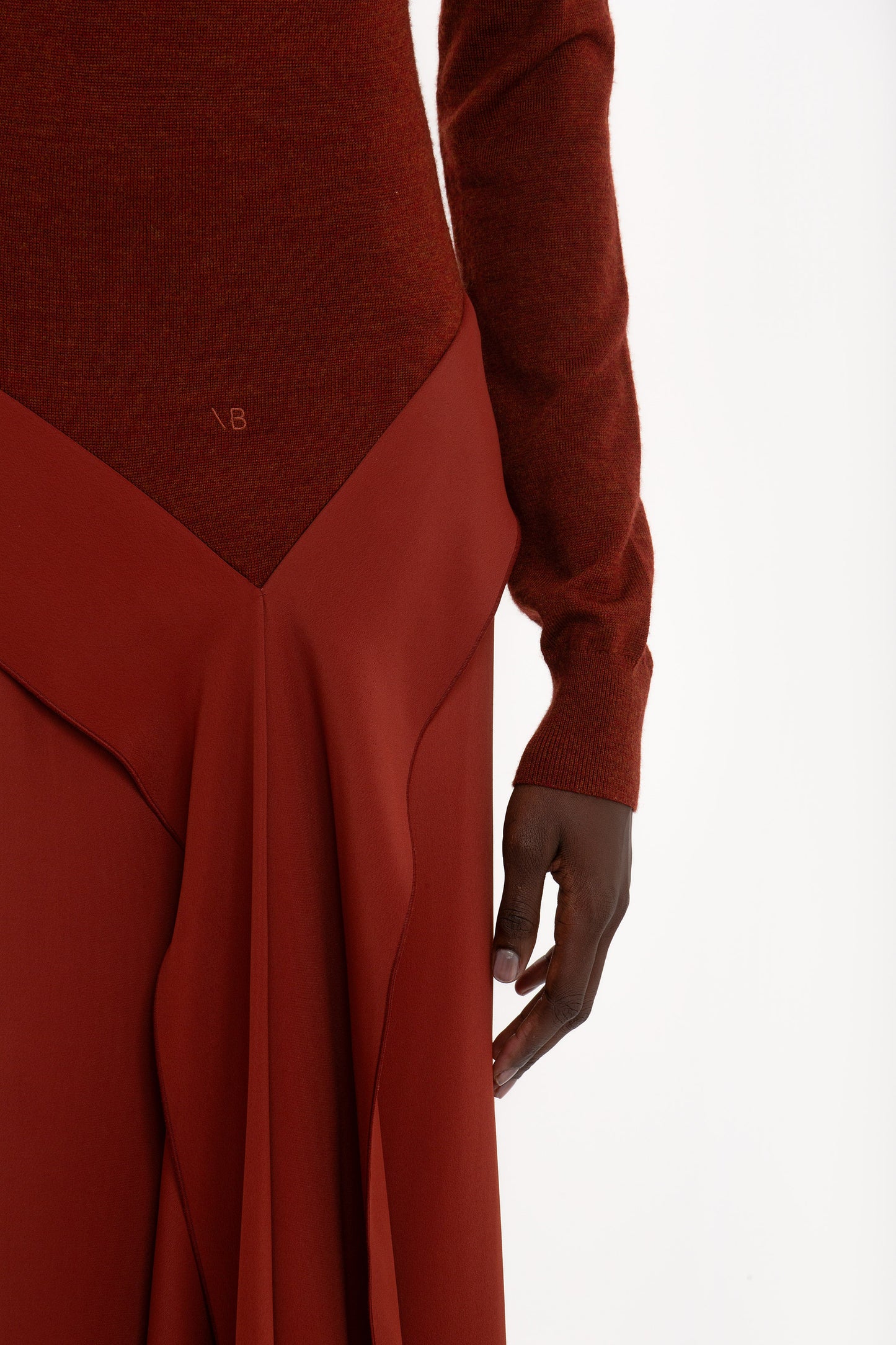 Close-up of a person wearing a Victoria Beckham High Neck Tie Detail Dress In Russet with long sleeves and a unique draped design detail. The image focuses on their hand and the lower part of this stylish High Neck Tie Detail Dress In Russet.