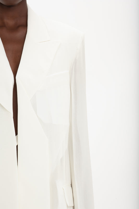 Close-up of an individual wearing a white, Fold Detail Tailored Jacket In White by Victoria Beckham with a notched lapel and subtle fold detail, set against a plain white background.