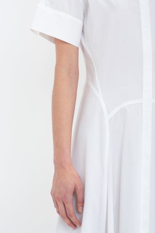 Close-up of a person wearing the Victoria Beckham Panelled Shirt Dress In White made from organic cotton poplin. Only the tailored design of the torso and arm are visible against a plain white background.
