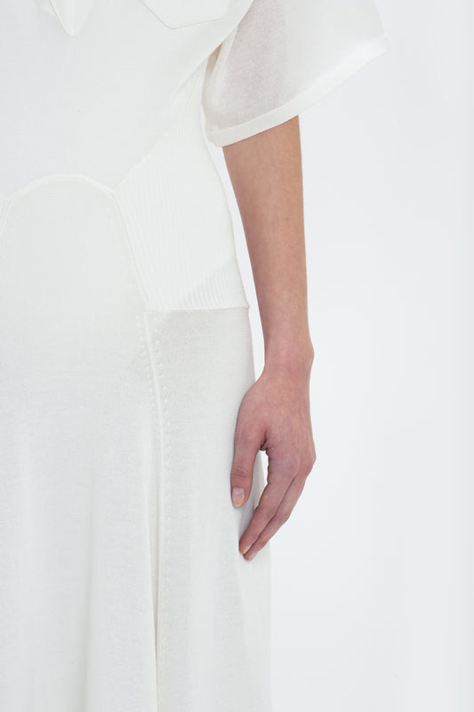 Close-up of a person wearing a Victoria Beckham Panelled Knit Dress In White, with only the lower arm and part of the midsection visible. The hand is relaxed and resting by their side, exuding relaxed glamour.
