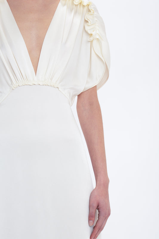 A close-up of a person wearing an Exclusive V-Neck Ruffle Midi Dress In Ivory with a deep neckline and ruffled sleeves by Victoria Beckham. The image focuses on the upper torso and right arm, against a plain white background, exuding an elegant Victoria Beckham style.